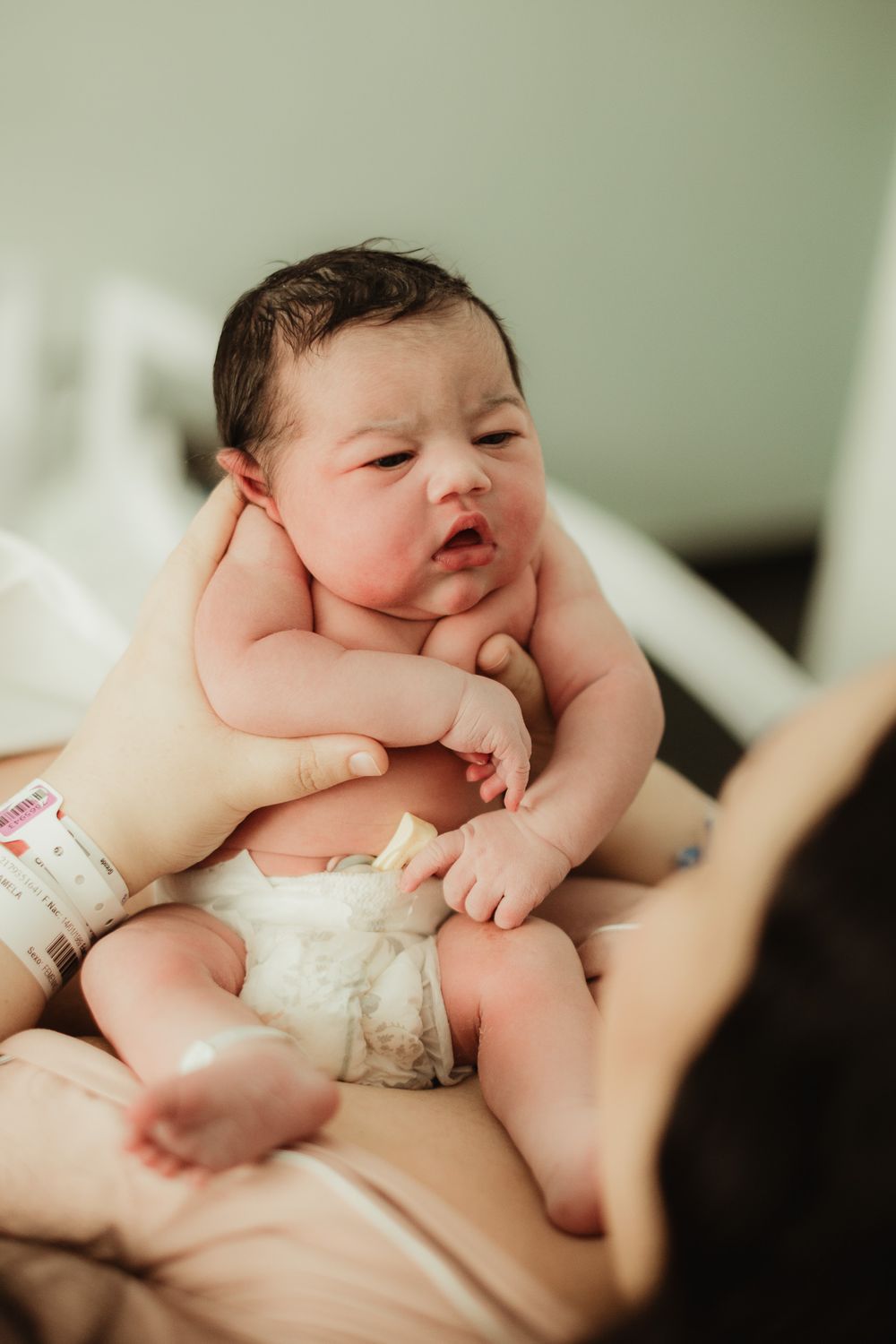 Newborn baby in diaper being held by mother in hospital room after birth.