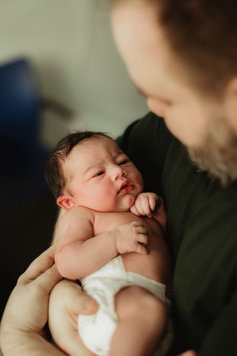 Bearded father tenderly holding his newborn baby in his arms indoors.