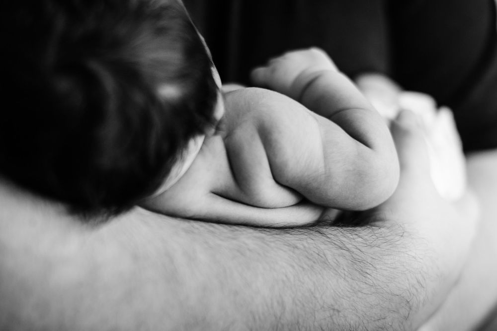 Black and white close-up of a newborn baby's tiny hand resting on a parent's arm.