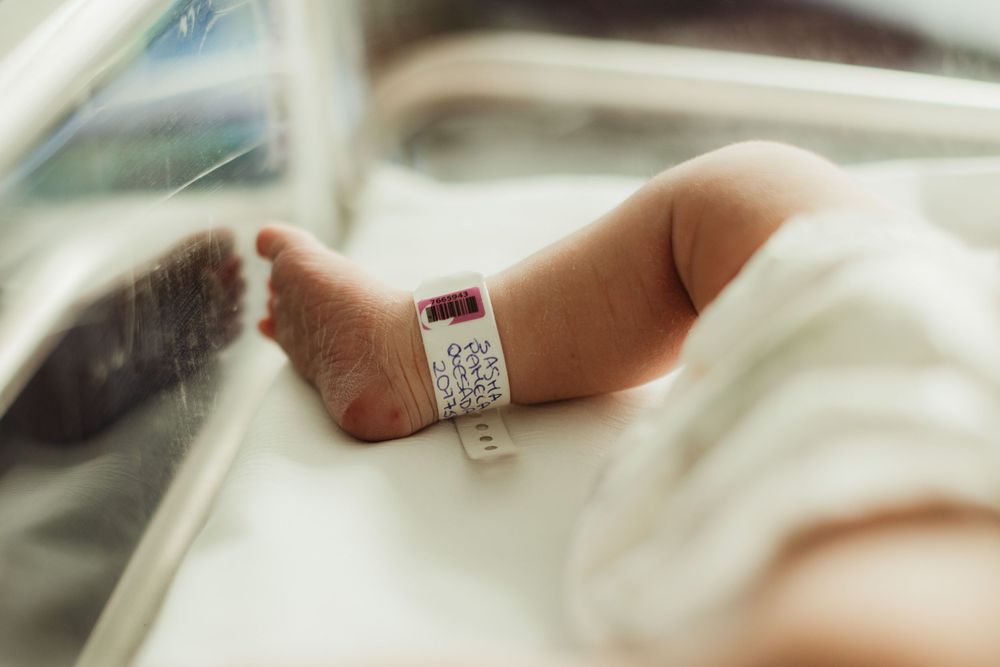 Newborn baby foot with hospital ID bracelet in a medical incubator, close-up maternity ward photo.