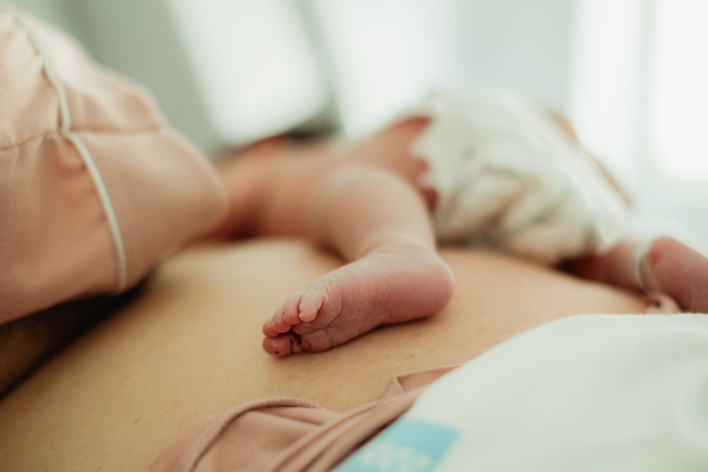 Newborn baby resting on mother's chest after birth, tiny feet visible in close-up skin-to-skin contact photo.