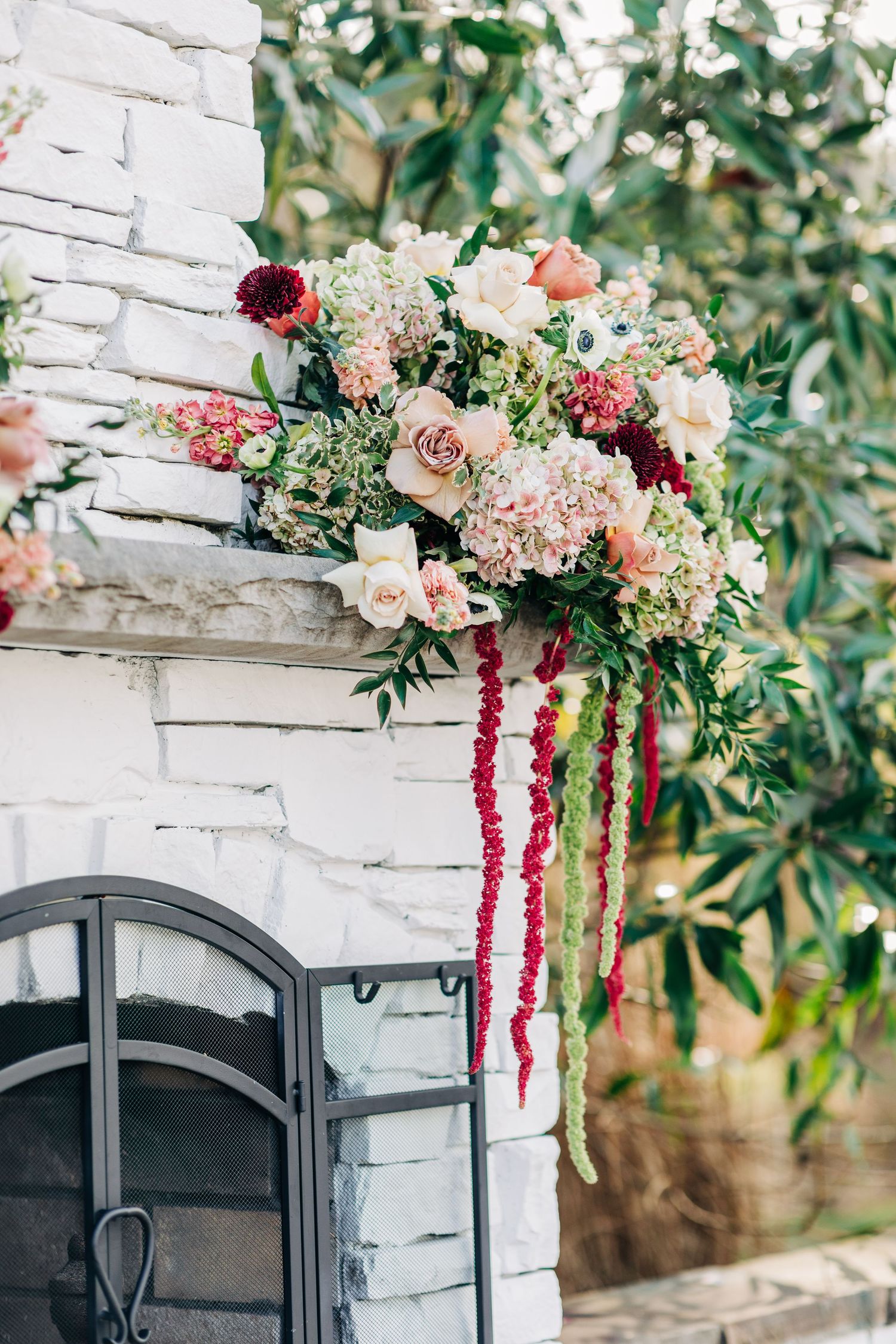 Elegant floral arrangement with pink and burgundy blooms cascades over a white stone wall with arched windows.