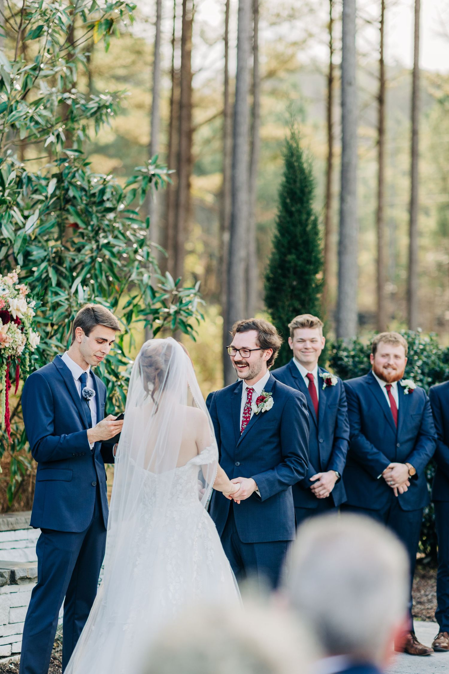 Wedding ceremony taking place outdoors with pine trees and natural greenery as the backdrop.