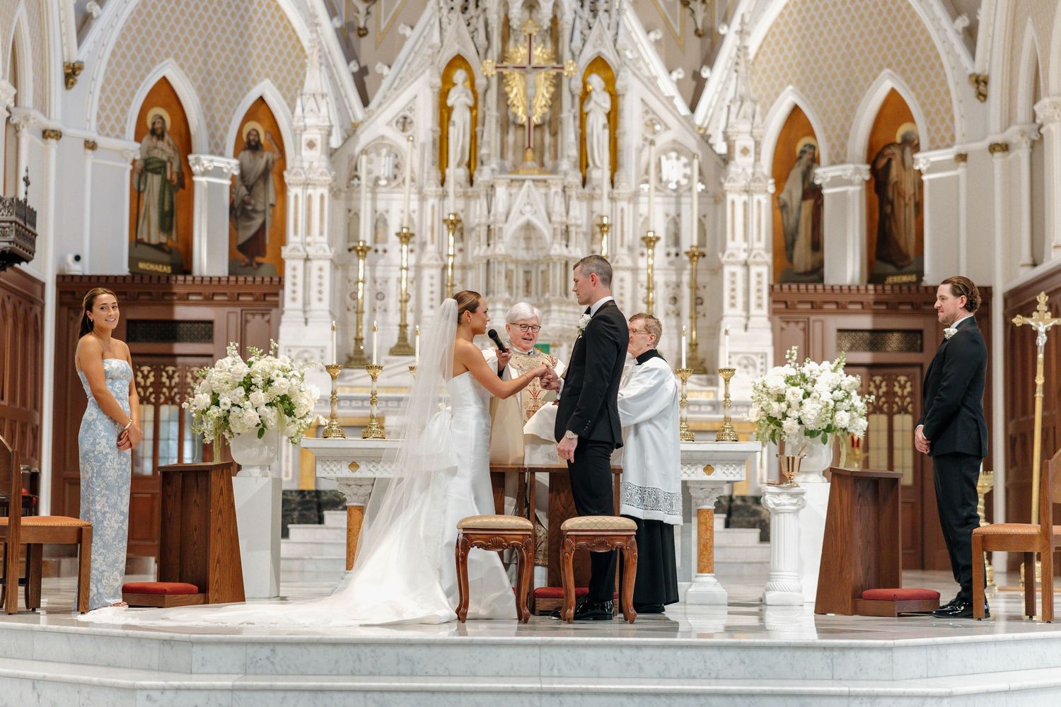 A grand cathedral interior with ornate white and gold architecture features tall columns and elegant arches during a ceremony.
