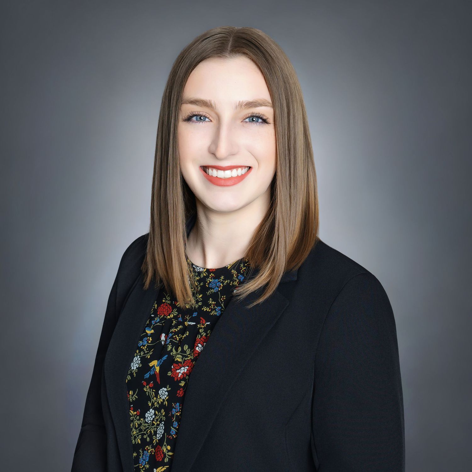 Professional headshot series showing confident woman in black blazer and dark top against gray backdrop with warm smile.