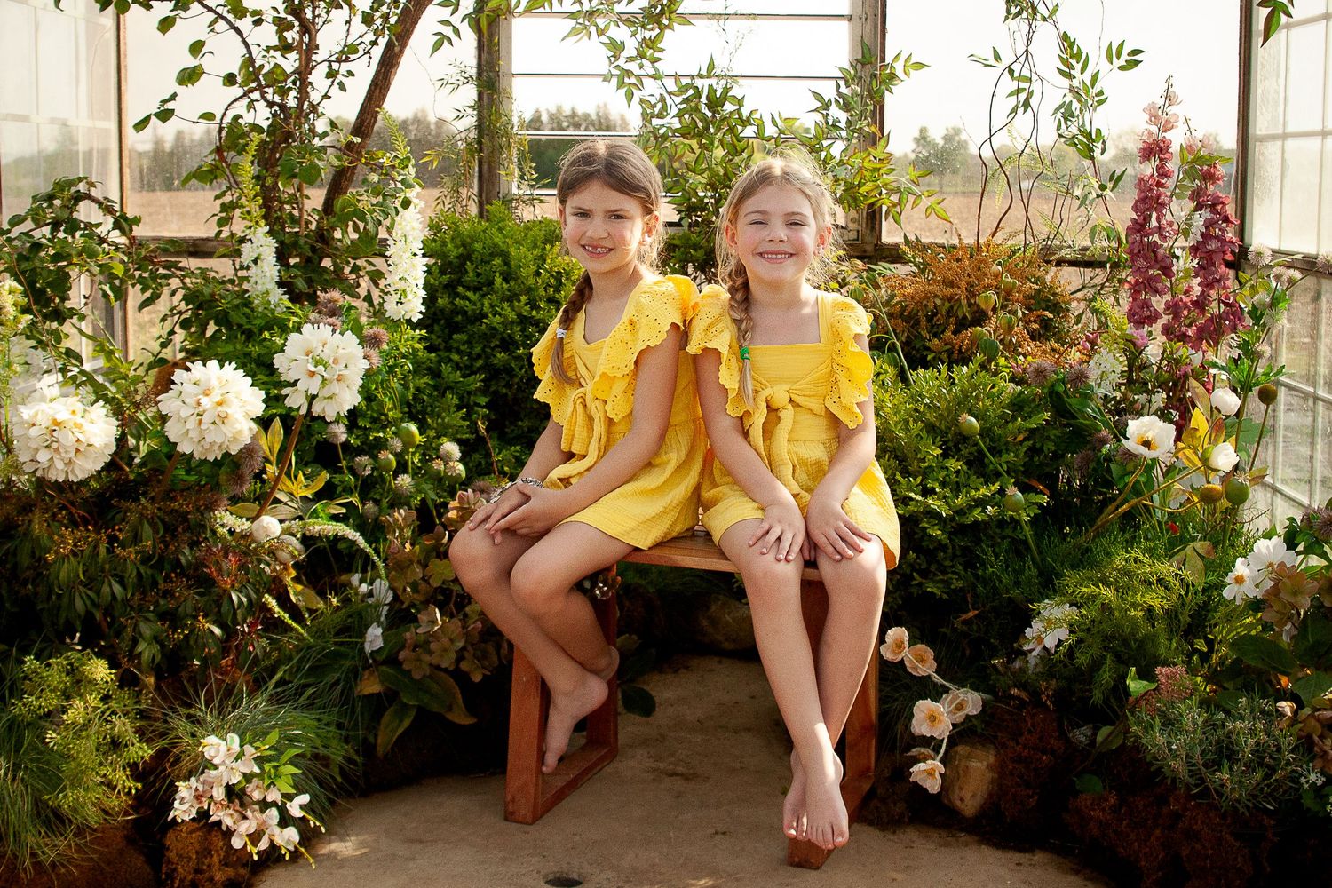 Family sitting together on outdoor bench surrounded by blooming pink and white flowers in a garden setting.