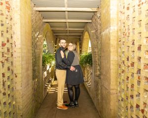 Couple standing in an archway corridor with brick walls covered in small colorful tiles or plaques.