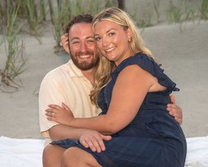Happy couple embracing on a sandy beach, woman in navy dress and man in cream polo shirt, smiling together outdoors.