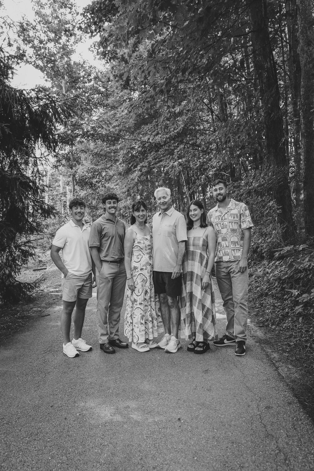 Black and white photo of six people posing together on a forest path surrounded by tall trees.
