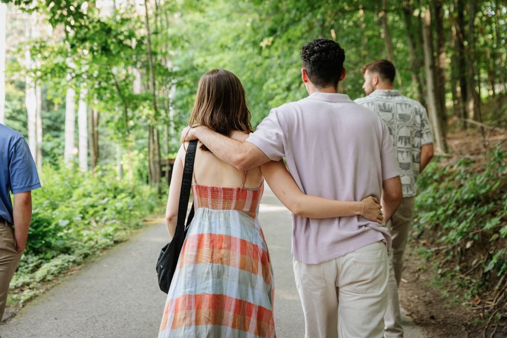 Couple walking arm in arm on a forest path surrounded by lush green trees.