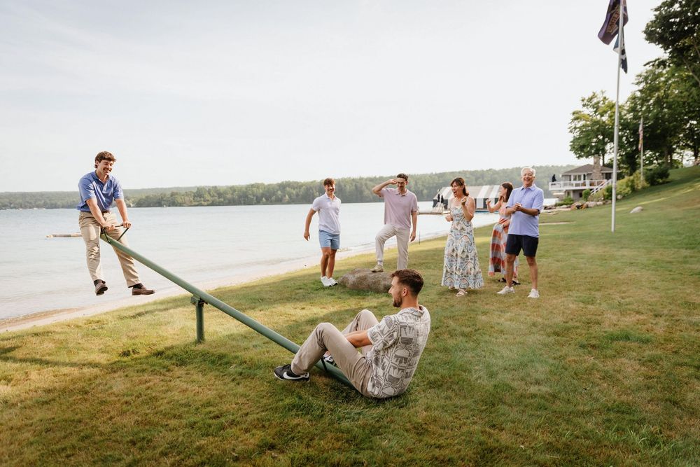 Group of friends enjoying outdoor lawn games by a lakeside on a sunny summer day.