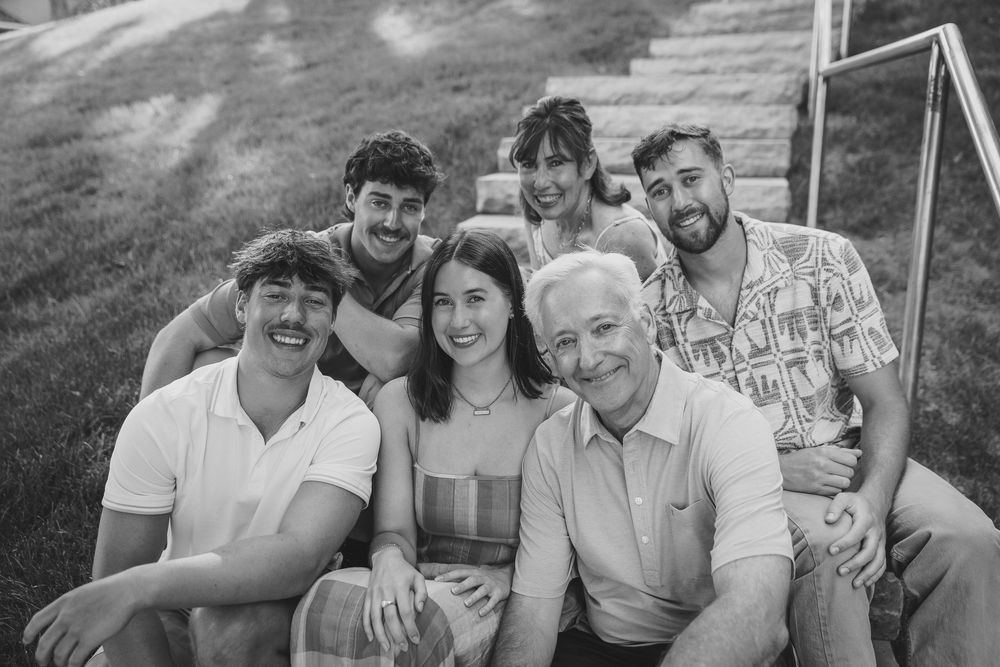 Black and white family portrait of six smiling people sitting on outdoor steps surrounded by green grass.