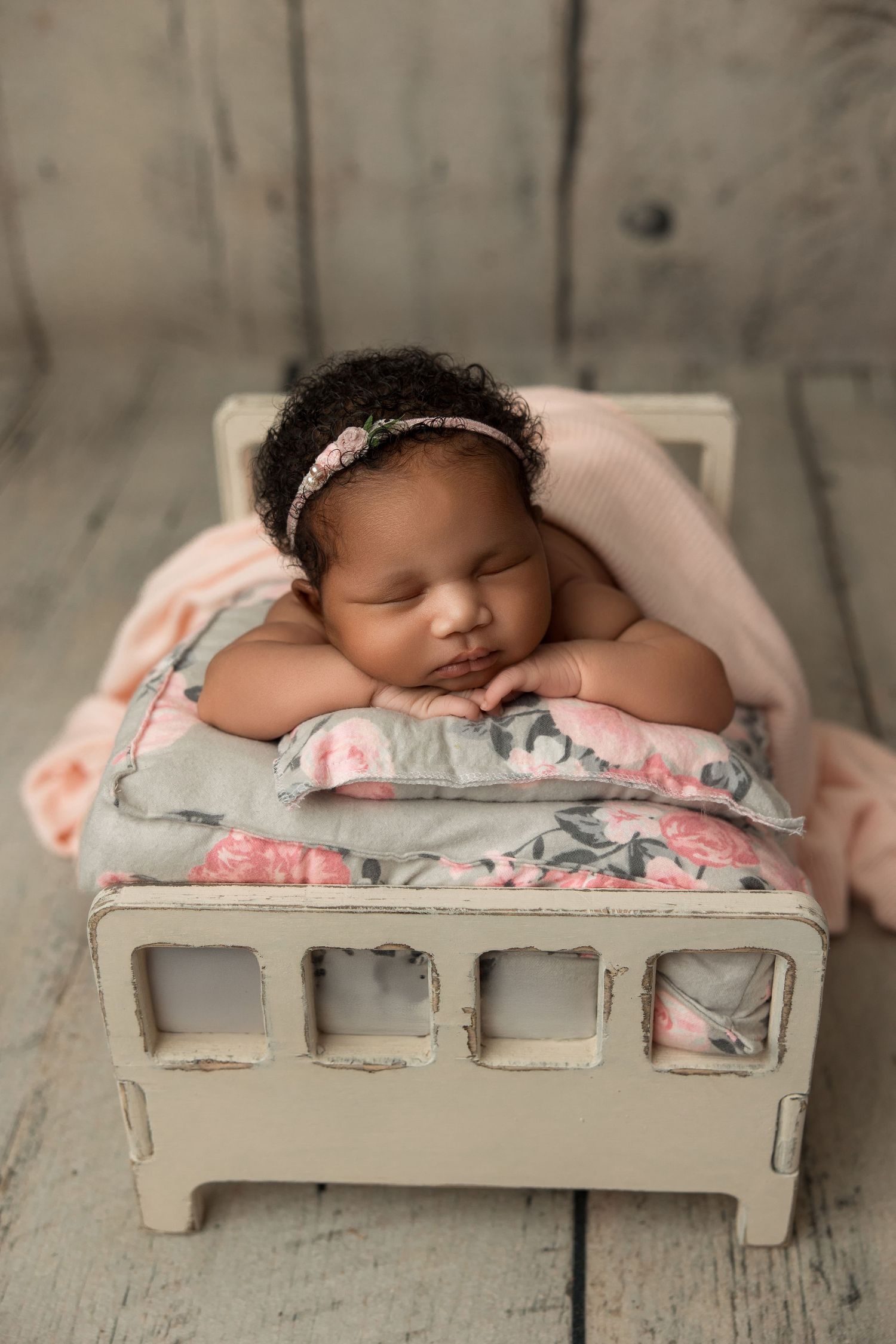 Sleeping newborn on white wooden bed with floral bedding in soft gray and pink tones.