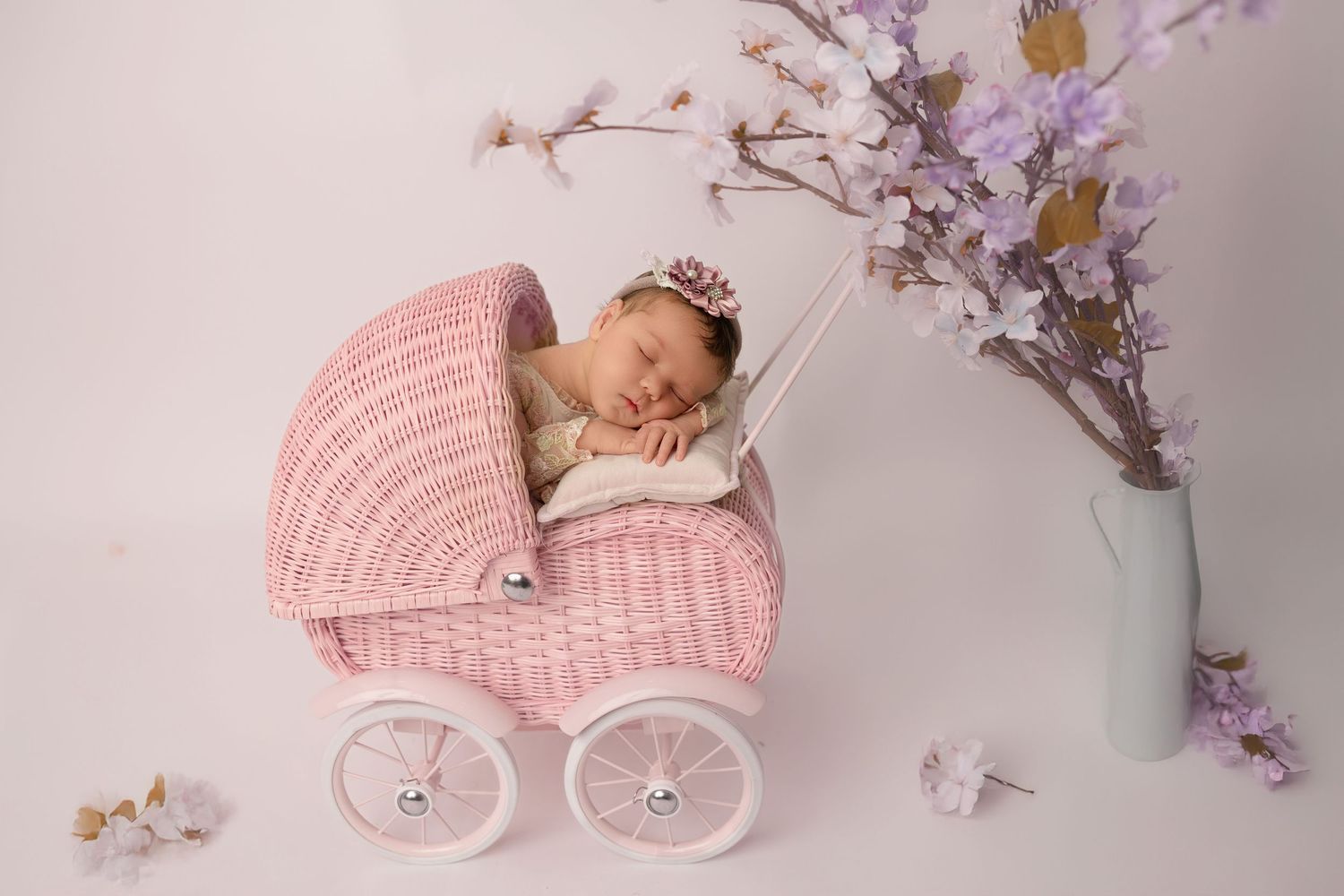 Pink vintage-style baby carriage with delicate floral decorations and cherry blossoms in a studio setting.