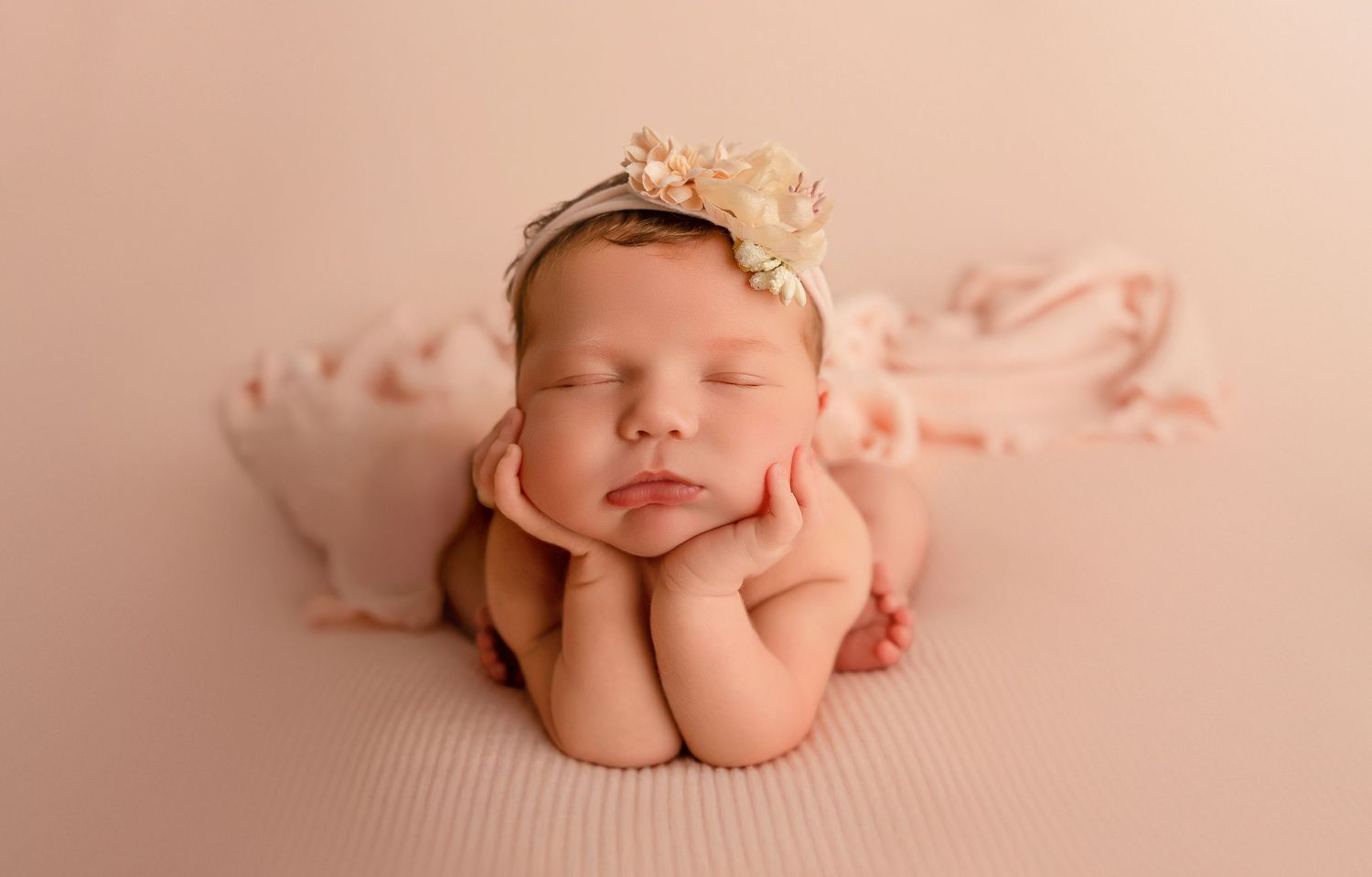 Newborn in peach tones wearing delicate headband posed on soft fabric background.