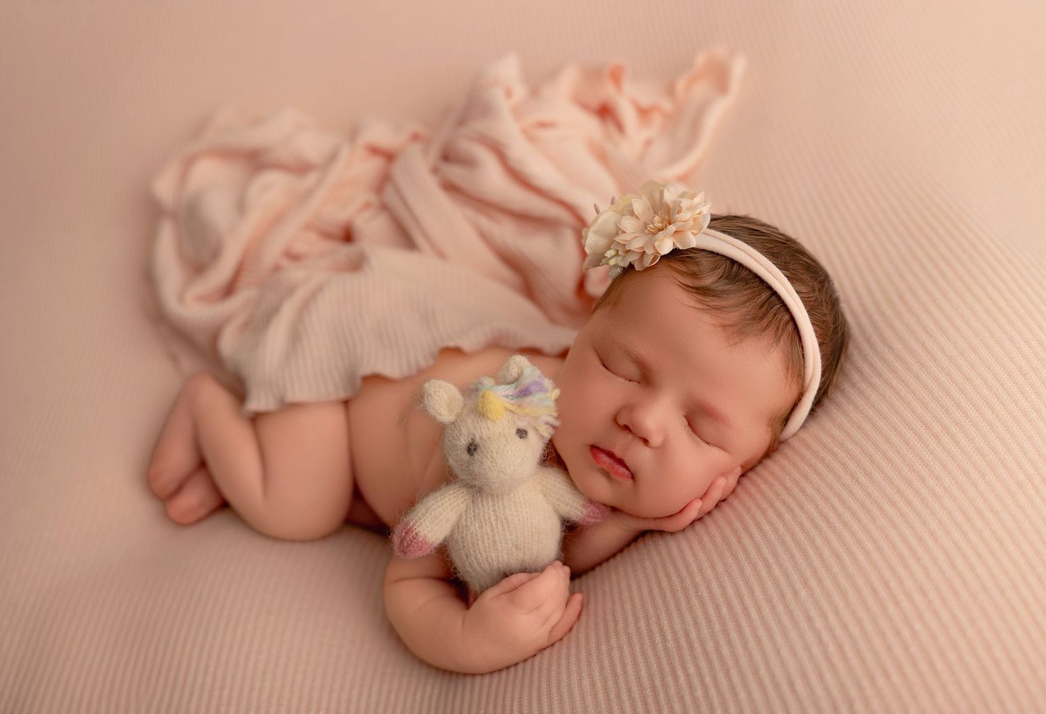 Peaceful newborn portrait on soft peach backdrop with gentle lighting and plush toy.