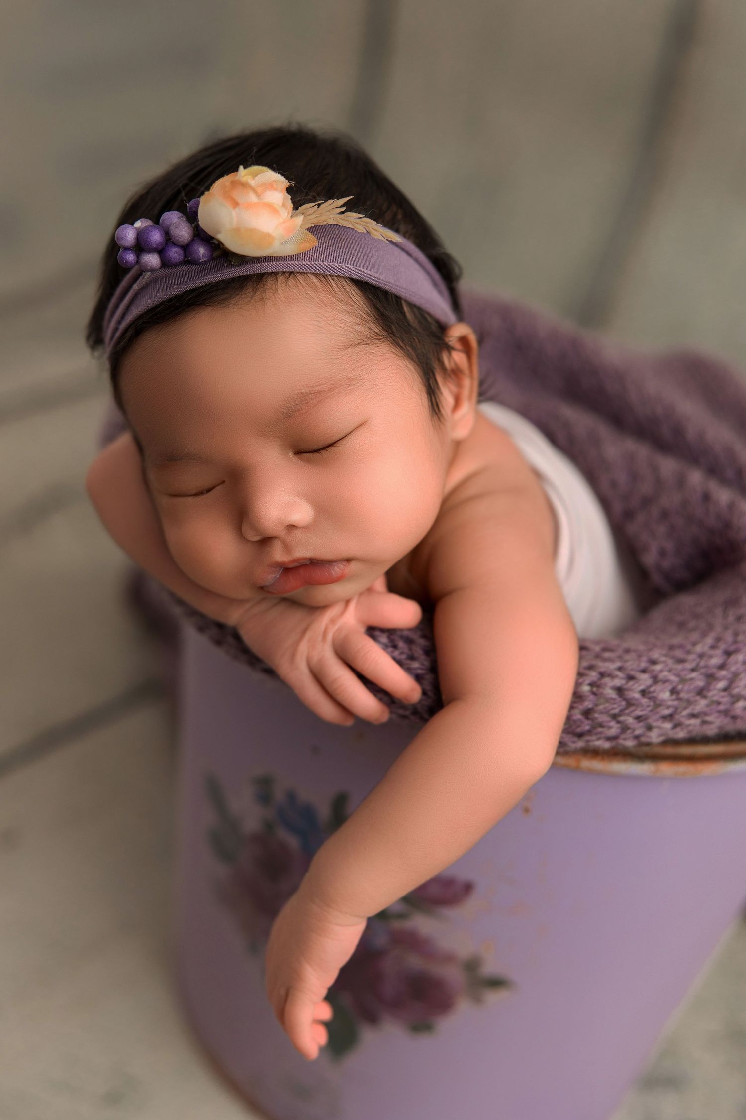 A sleeping baby wrapped in purple blankets rests peacefully in a cozy studio photography setup.