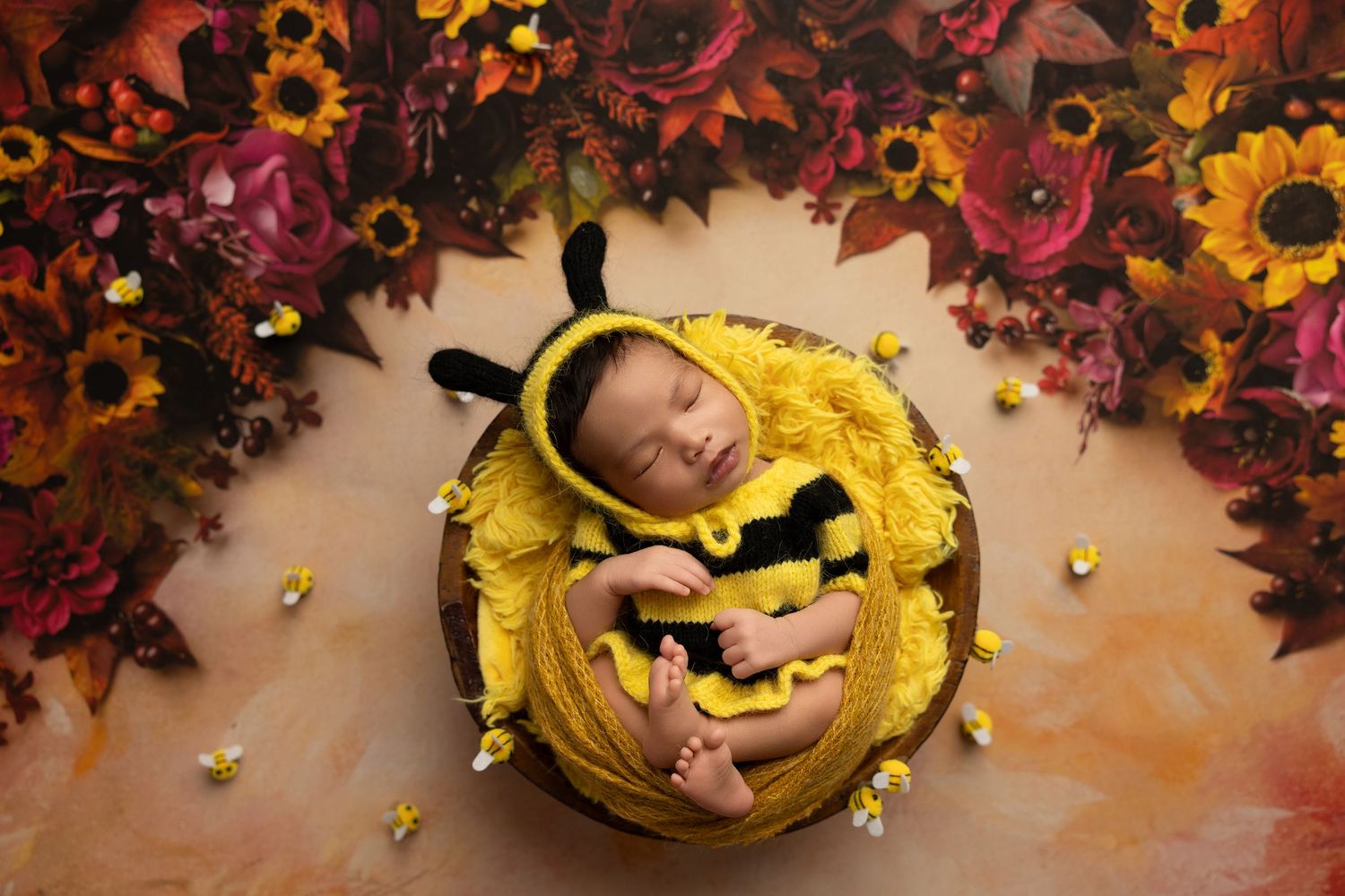 A sleeping baby nestled in a bright yellow sunflower-themed setting with autumn leaves in the background.