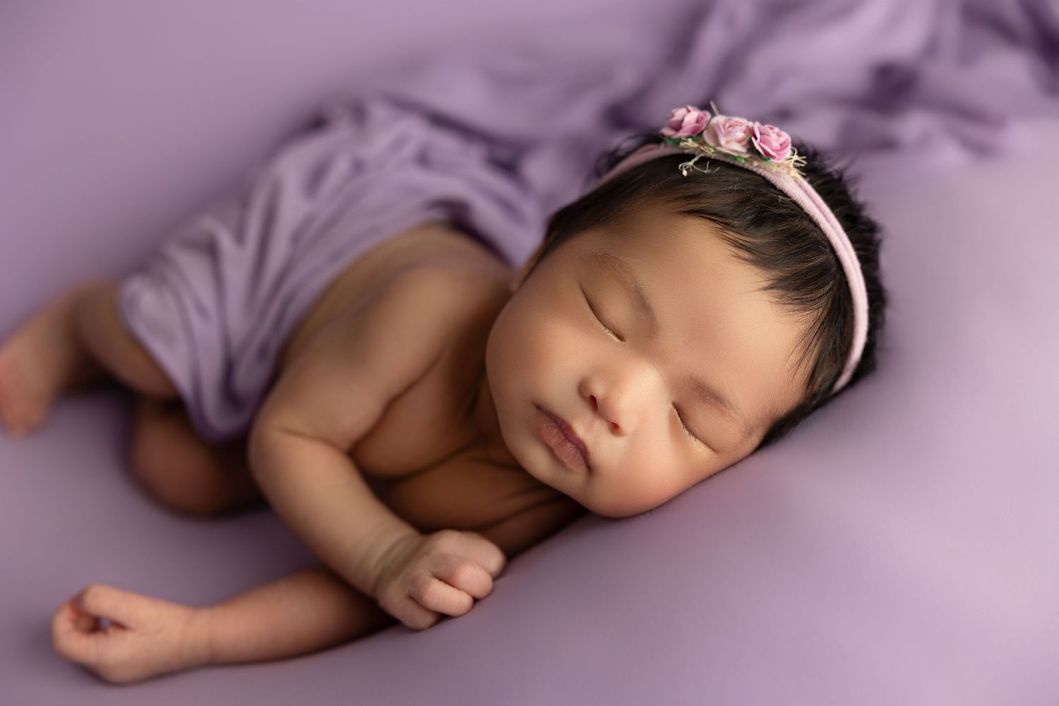 Sleeping newborn baby in purple swaddle cloth lying on soft blanket in various peaceful sleeping positions.