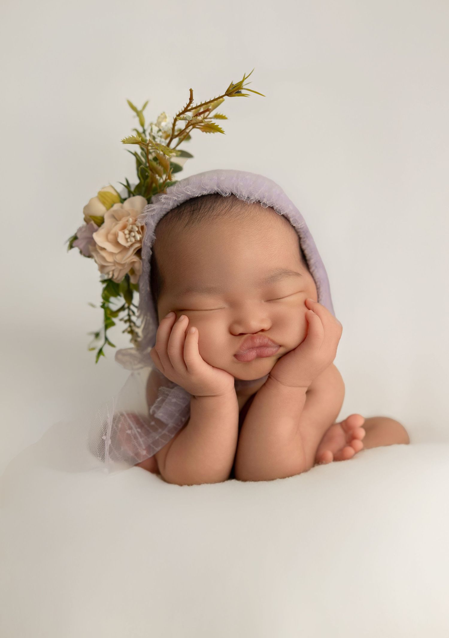 A delicate newborn photography session features a sleeping baby adorned with soft pink flowers and lavender accessories.