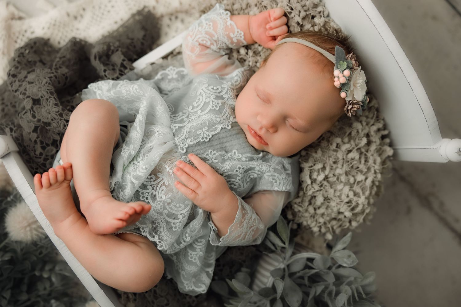 A baby wearing a silver-gray dress lies on a gray textured surface in a series of connected photos.