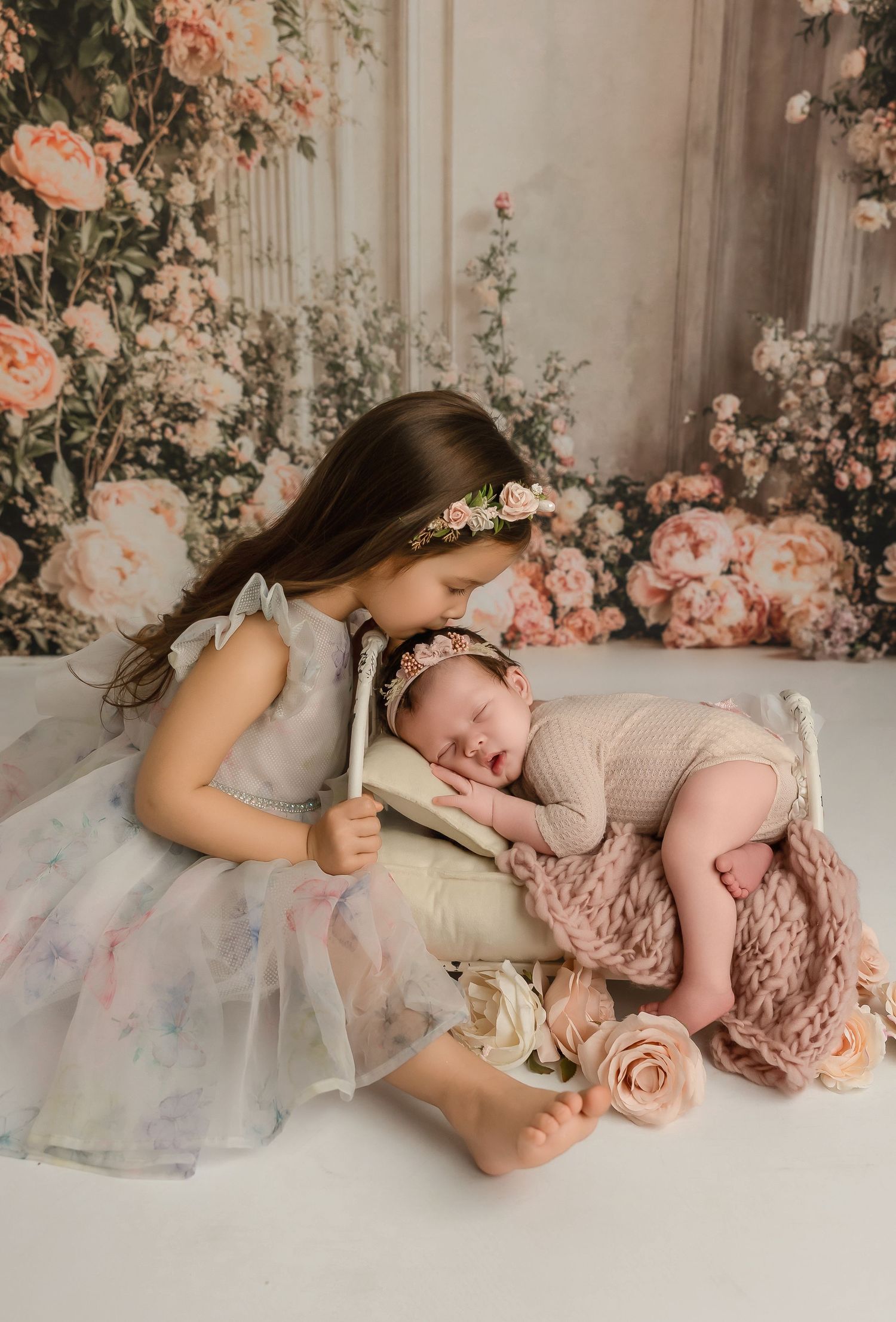 A tender newborn photography session featuring soft pink floral arrangements and delicate poses in a dreamy studio setting.