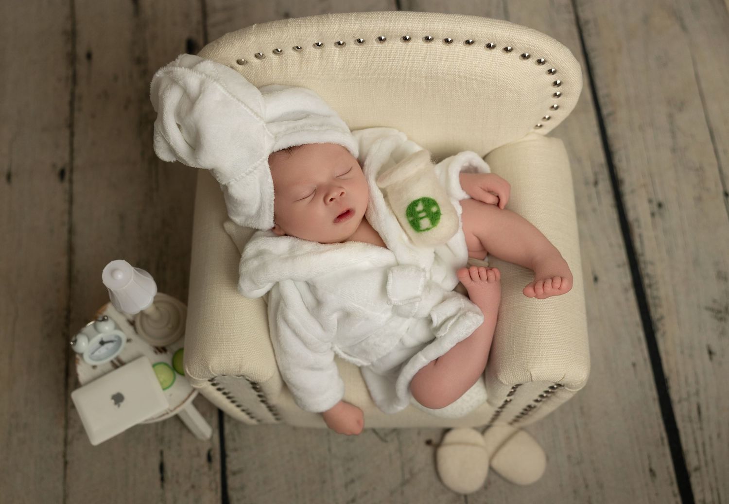 Sleeping newborn baby wearing white outfit lies on soft beige blanket in professional studio setting.