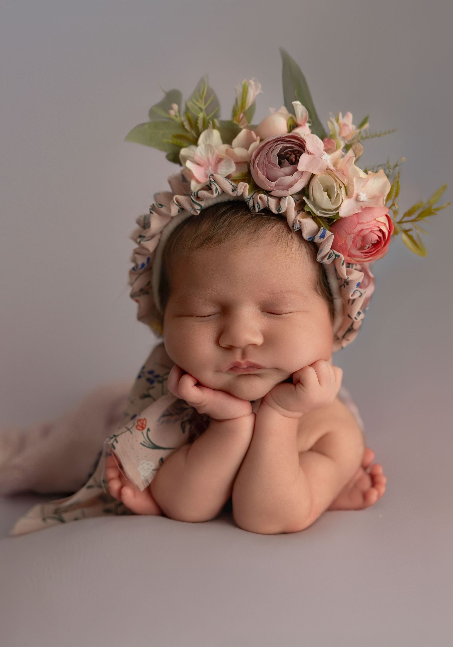 A sleeping newborn wearing a delicate floral crown lies peacefully in different poses against a soft gray backdrop.