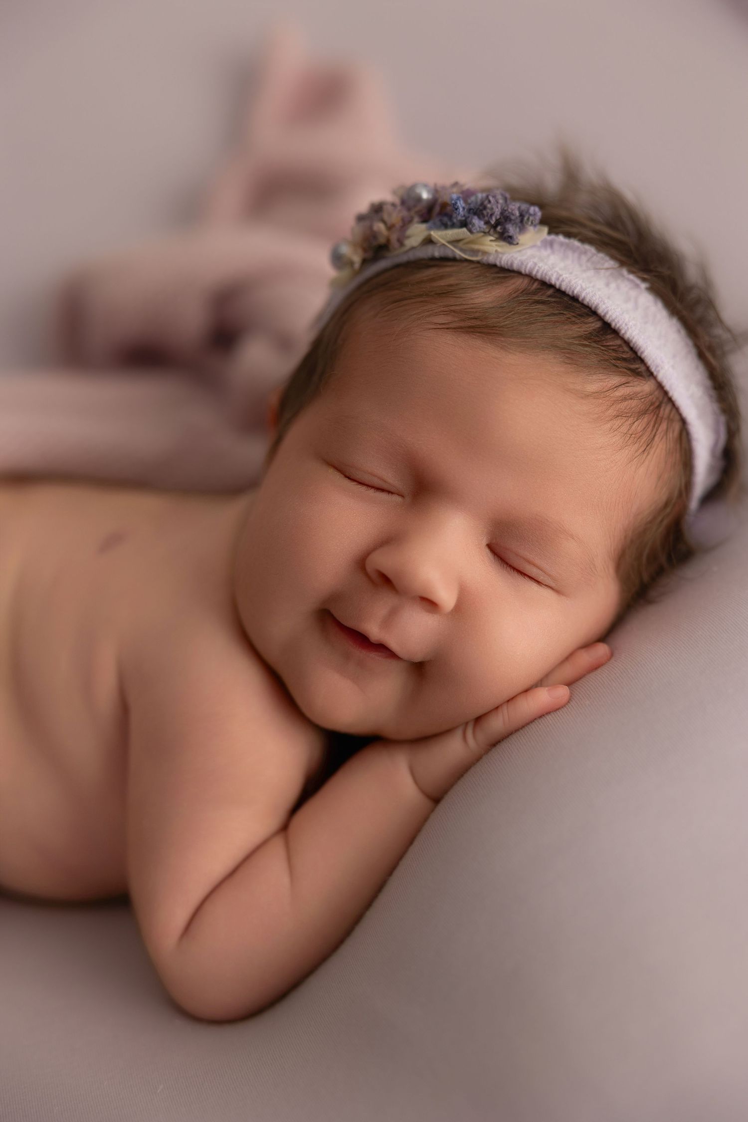 Peaceful sleeping newborn baby wearing delicate lace headband rests on soft pink blanket in artistic portrait series.