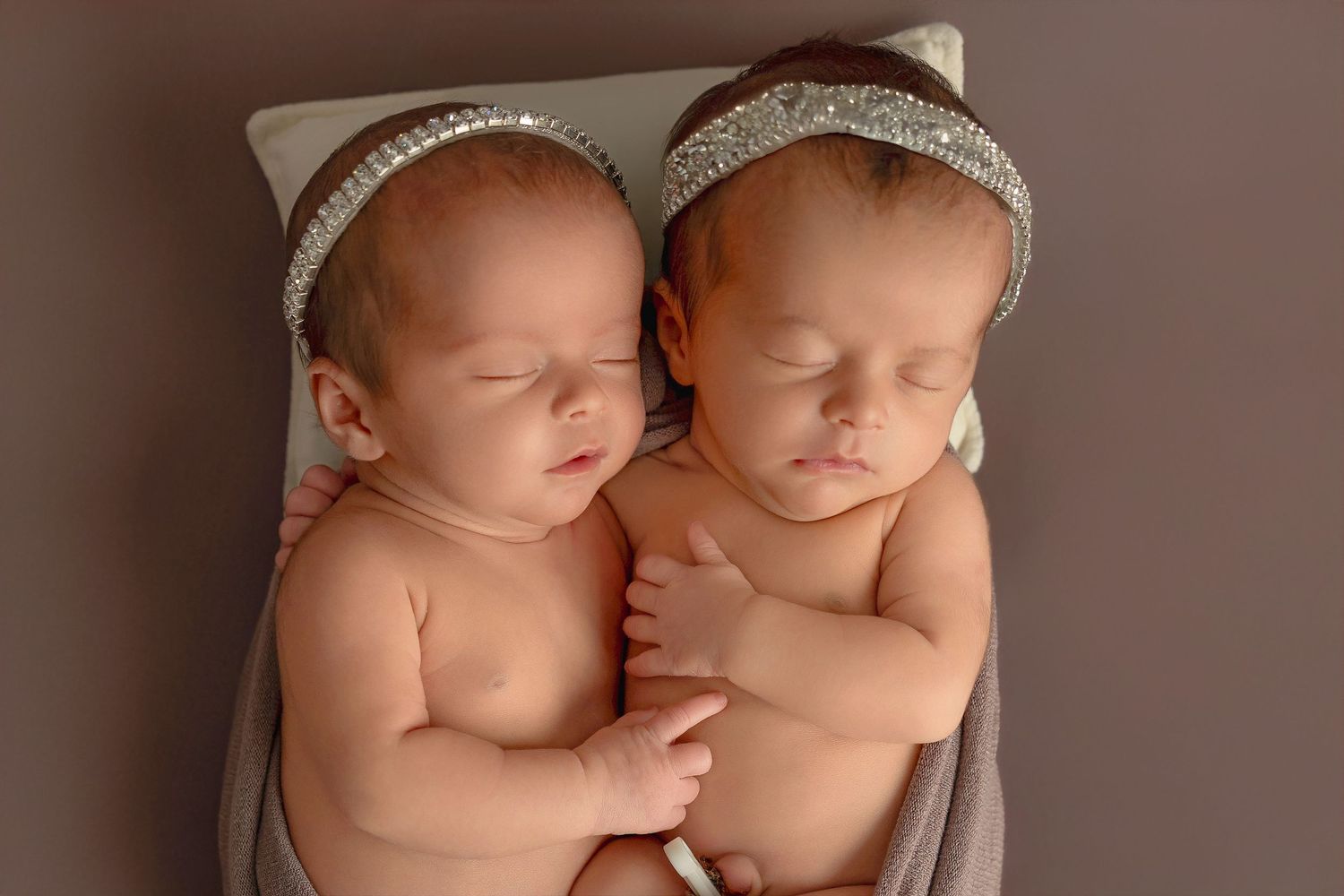 Two sleeping newborn babies wearing matching knit hats rest together in a tender pose during a professional photo session.