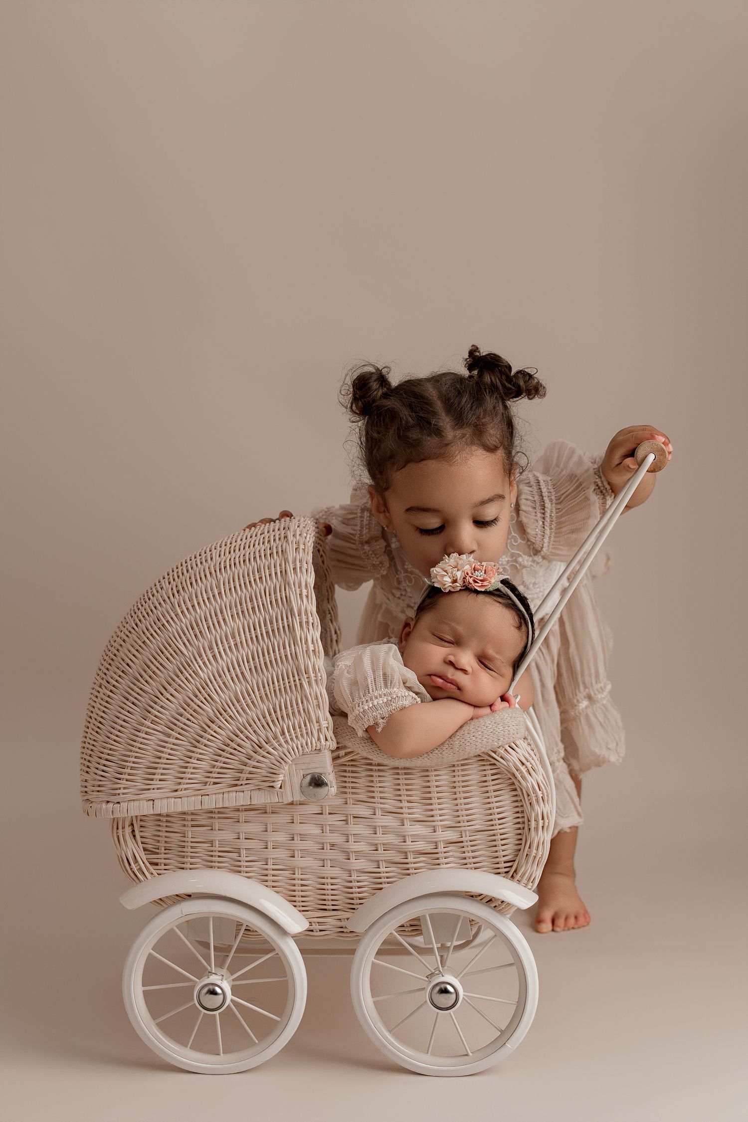 A vintage-style white wicker doll carriage with a sleeping baby and companion in matching white lace outfits.