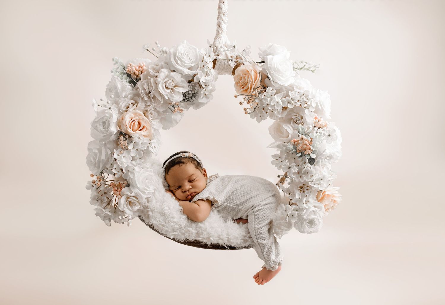 A baby lies peacefully surrounded by white Christmas decorations and twinkling lights in a festive holiday portrait.