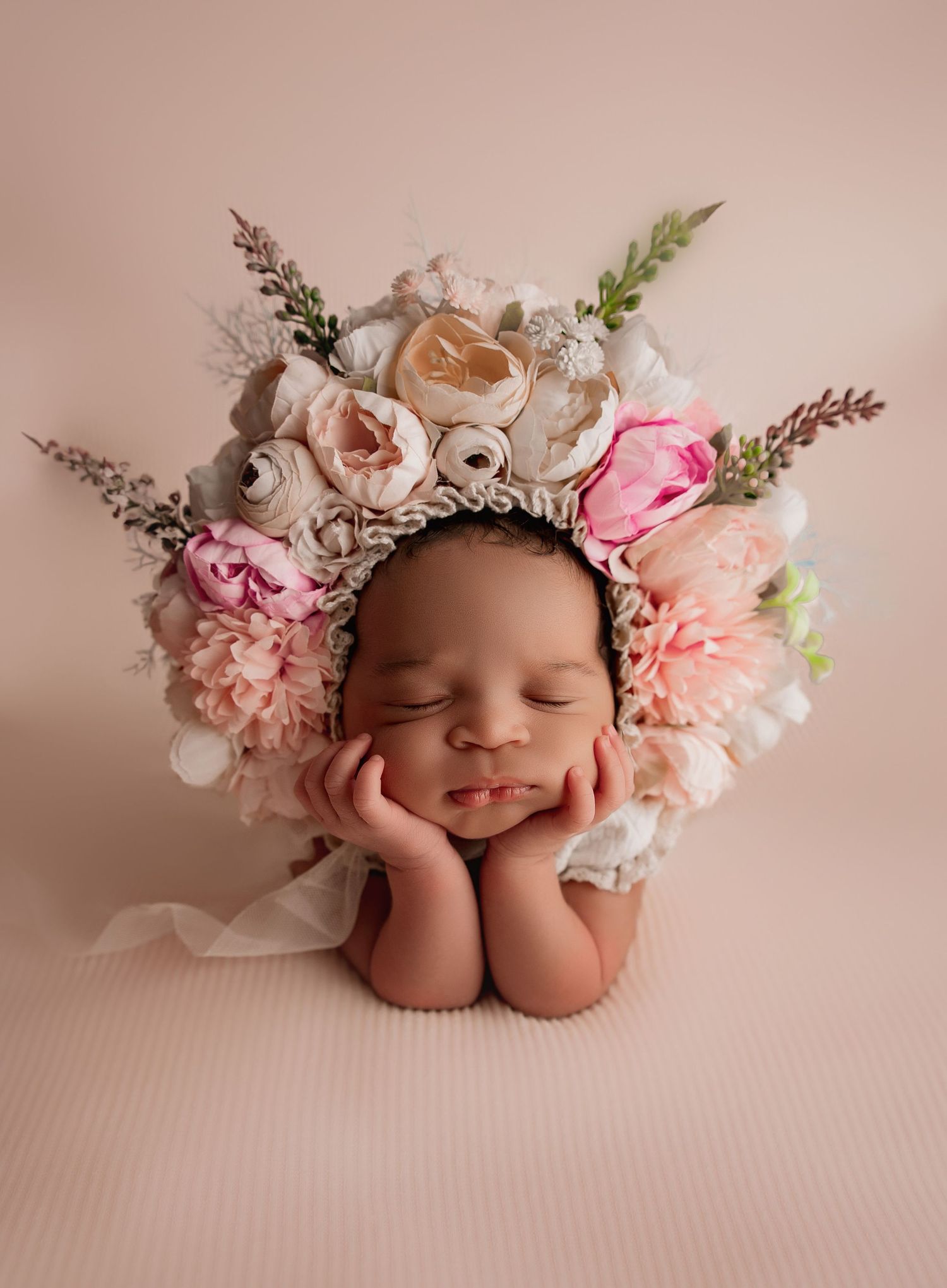 A sleeping newborn adorned with delicate pink and white floral crown poses peacefully on a soft pink backdrop.