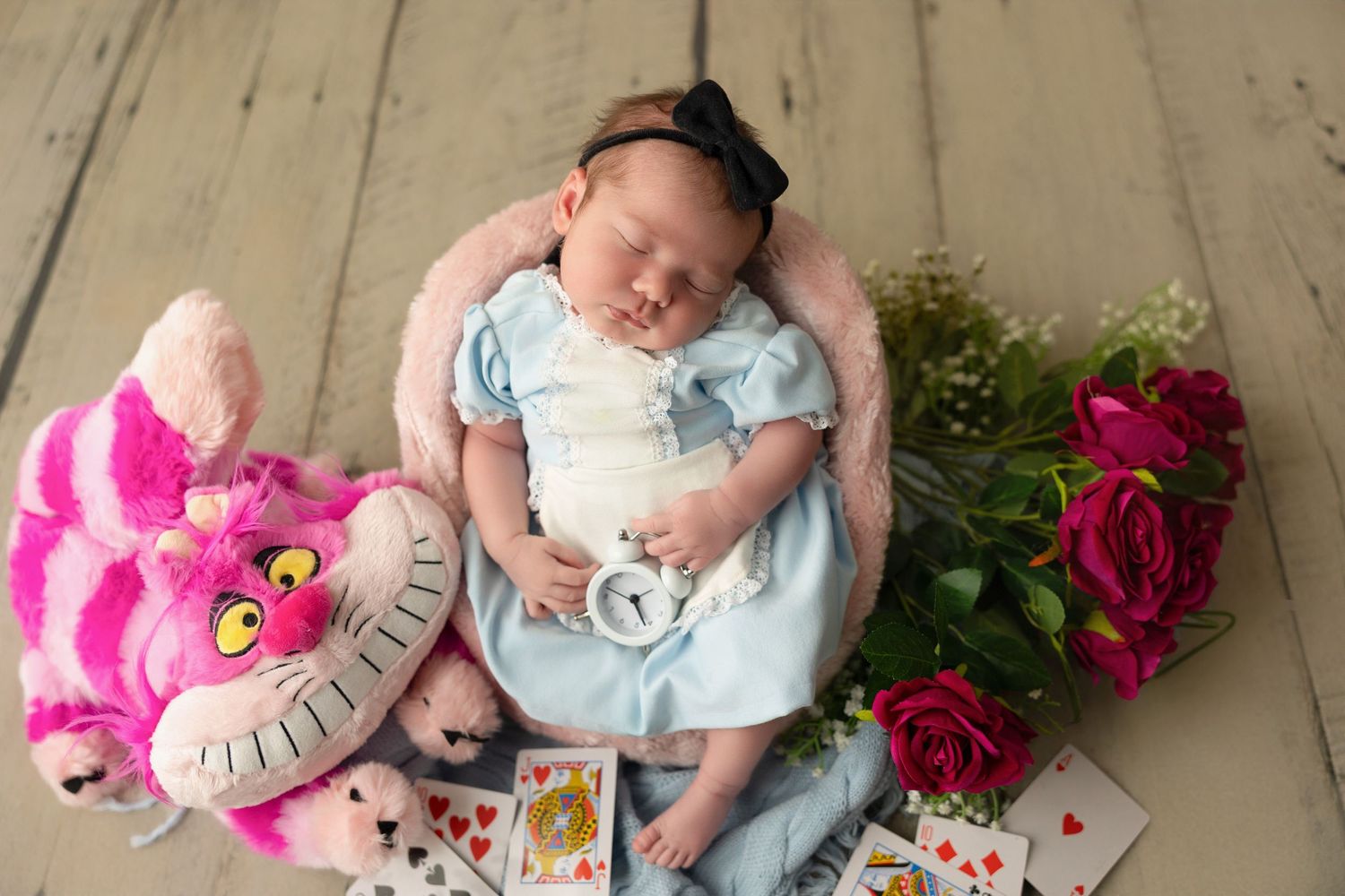 Baby lies on wooden floor with pink heart pillow and roses in monthly milestone photo series.