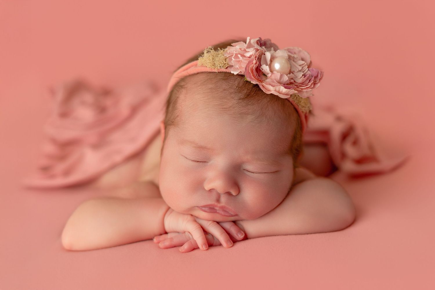 Sleeping newborn baby wrapped in soft pink fabric lying on a pink backdrop during professional photo session.