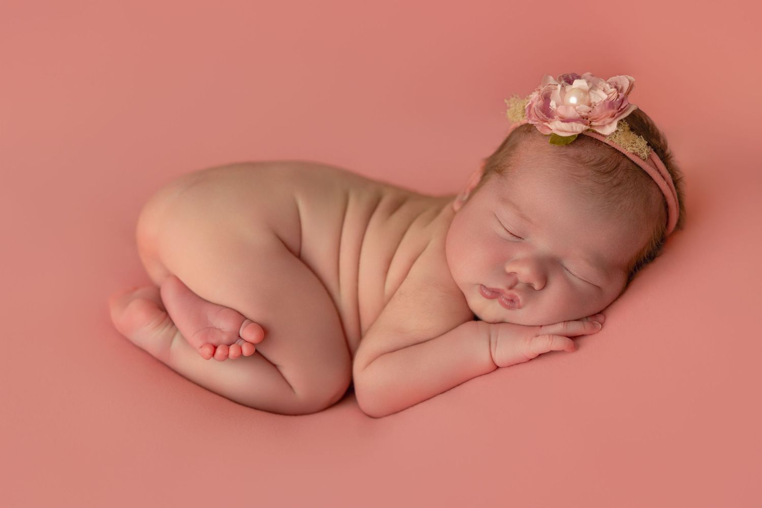 A sleeping newborn baby lies on a soft pink background in a series of peaceful poses.