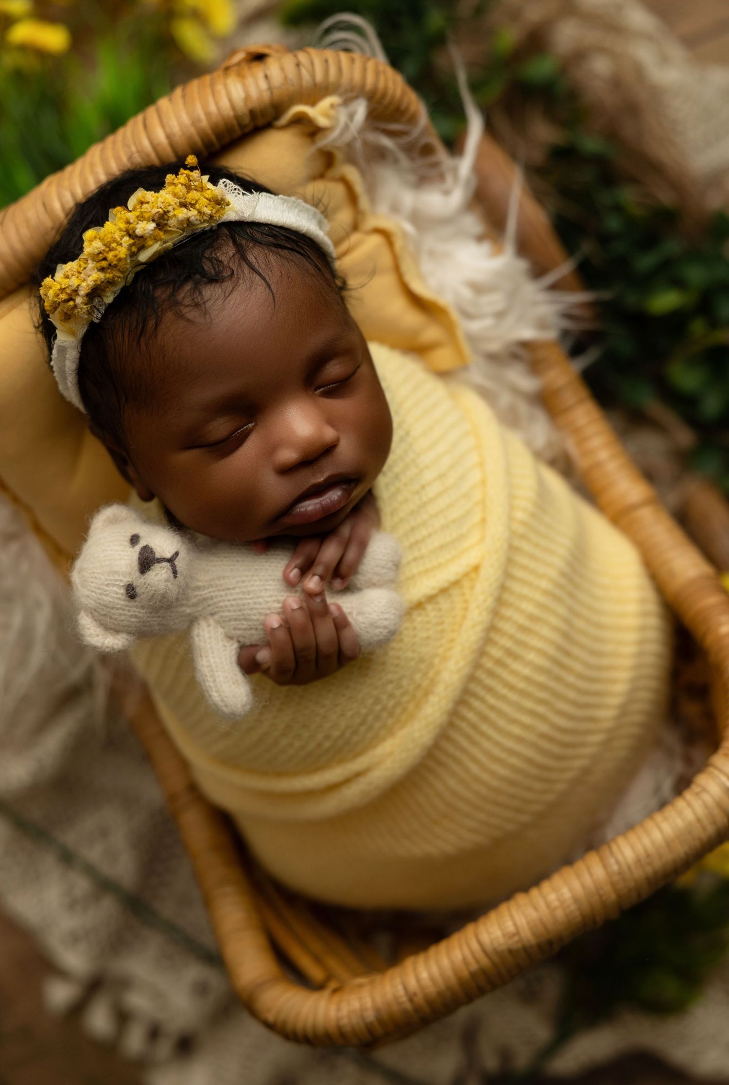 Sleeping baby wearing a cozy yellow sweater rests peacefully in a wicker basket outdoors.
