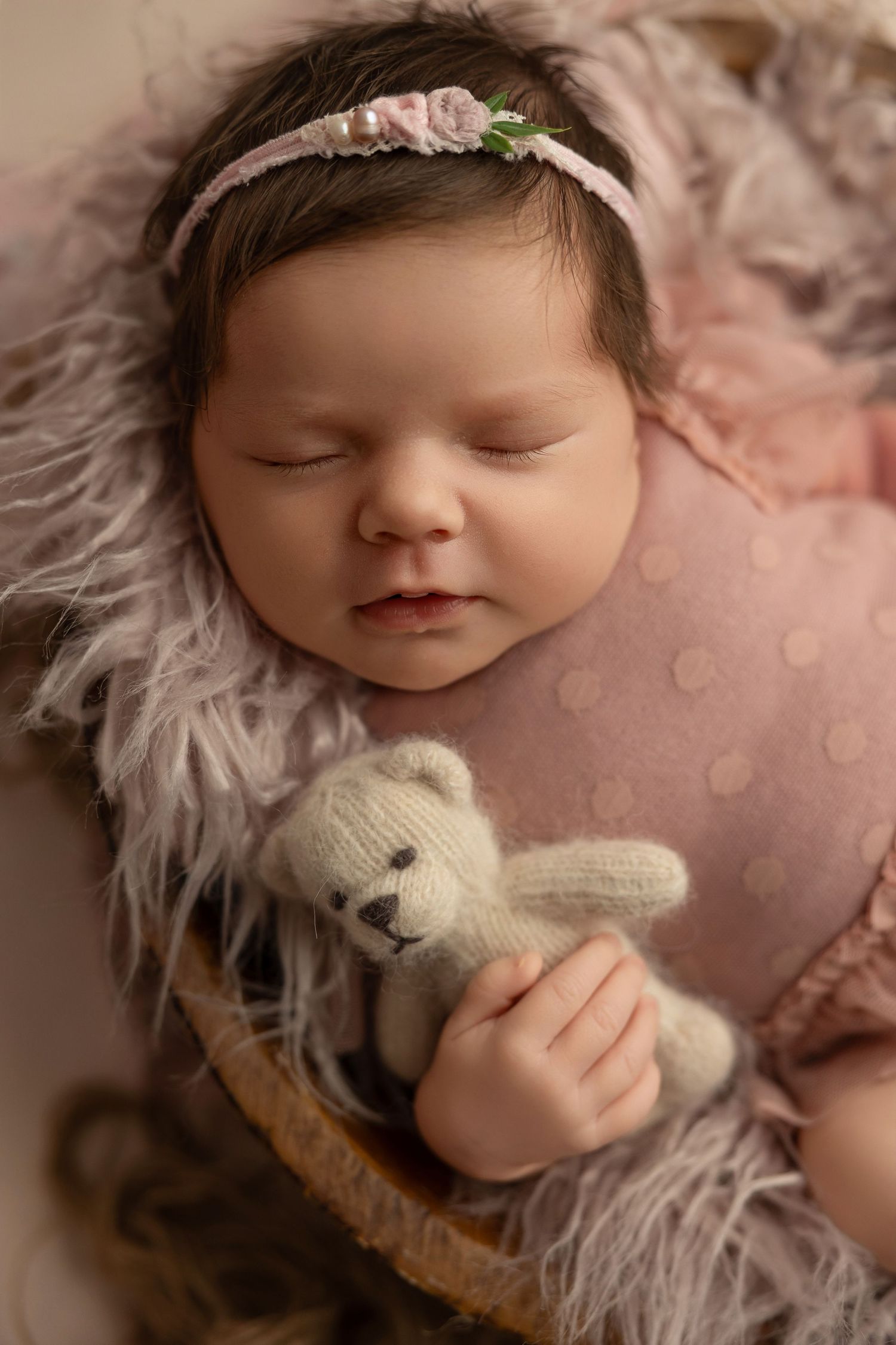 A peaceful newborn baby sleeping on soft pink fur with a small white plush bunny toy.