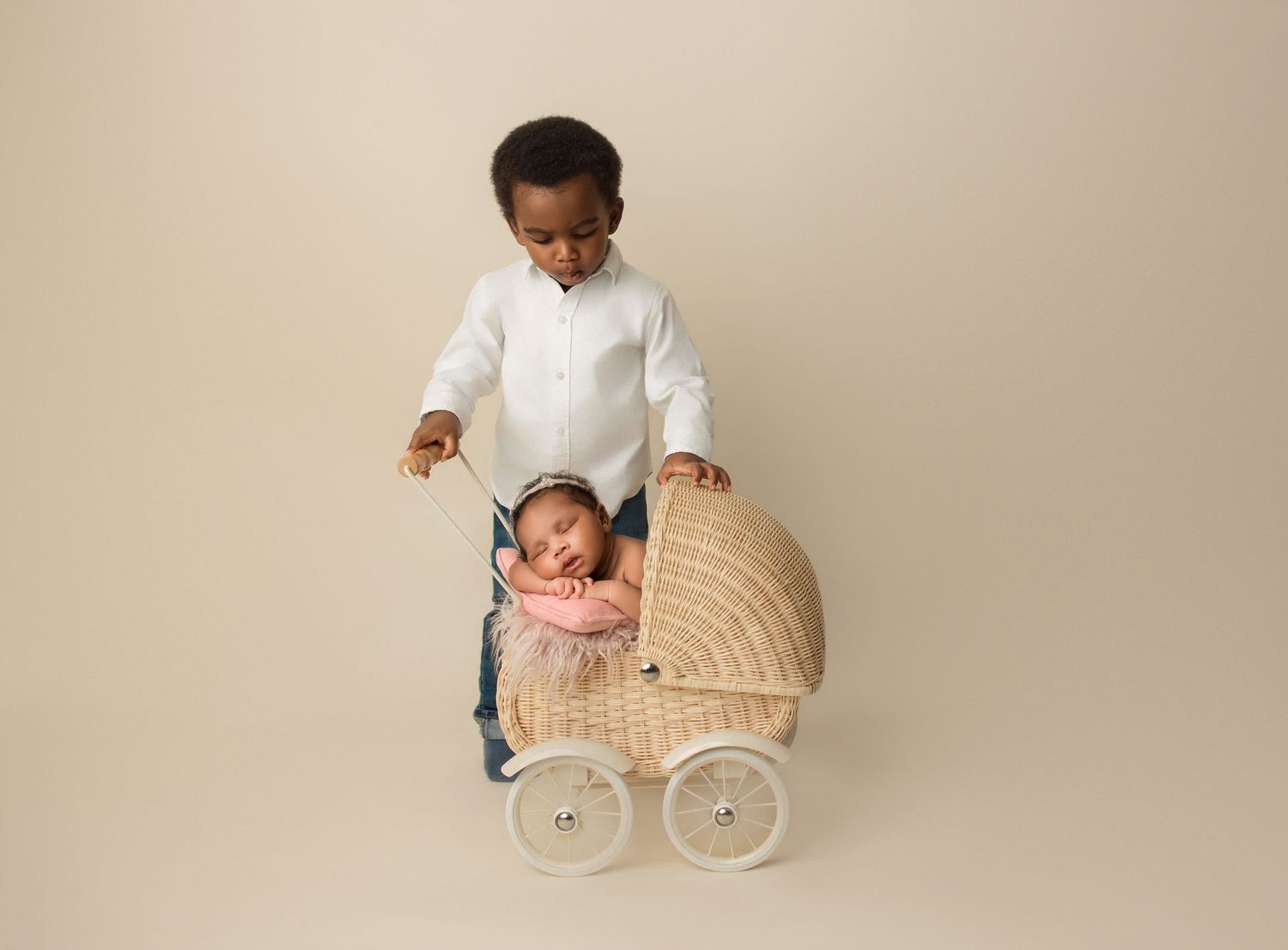 Children playing with vintage-style wicker baby carriage against neutral backdrop.