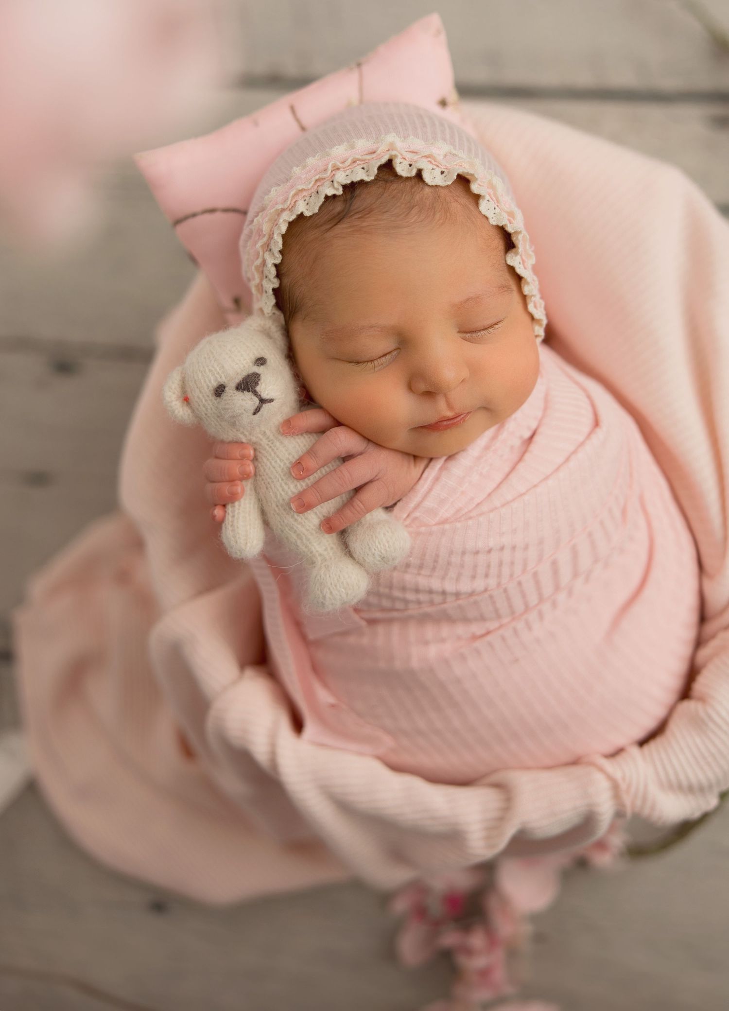 Sleeping newborn wrapped in soft pink blanket with delicate lace headband in professional studio portrait series.