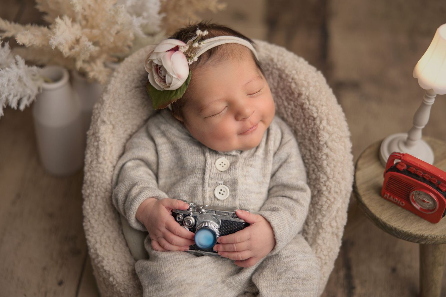 Peaceful newborn resting in cozy grey basket surrounded by vintage decorative elements in studio setting.