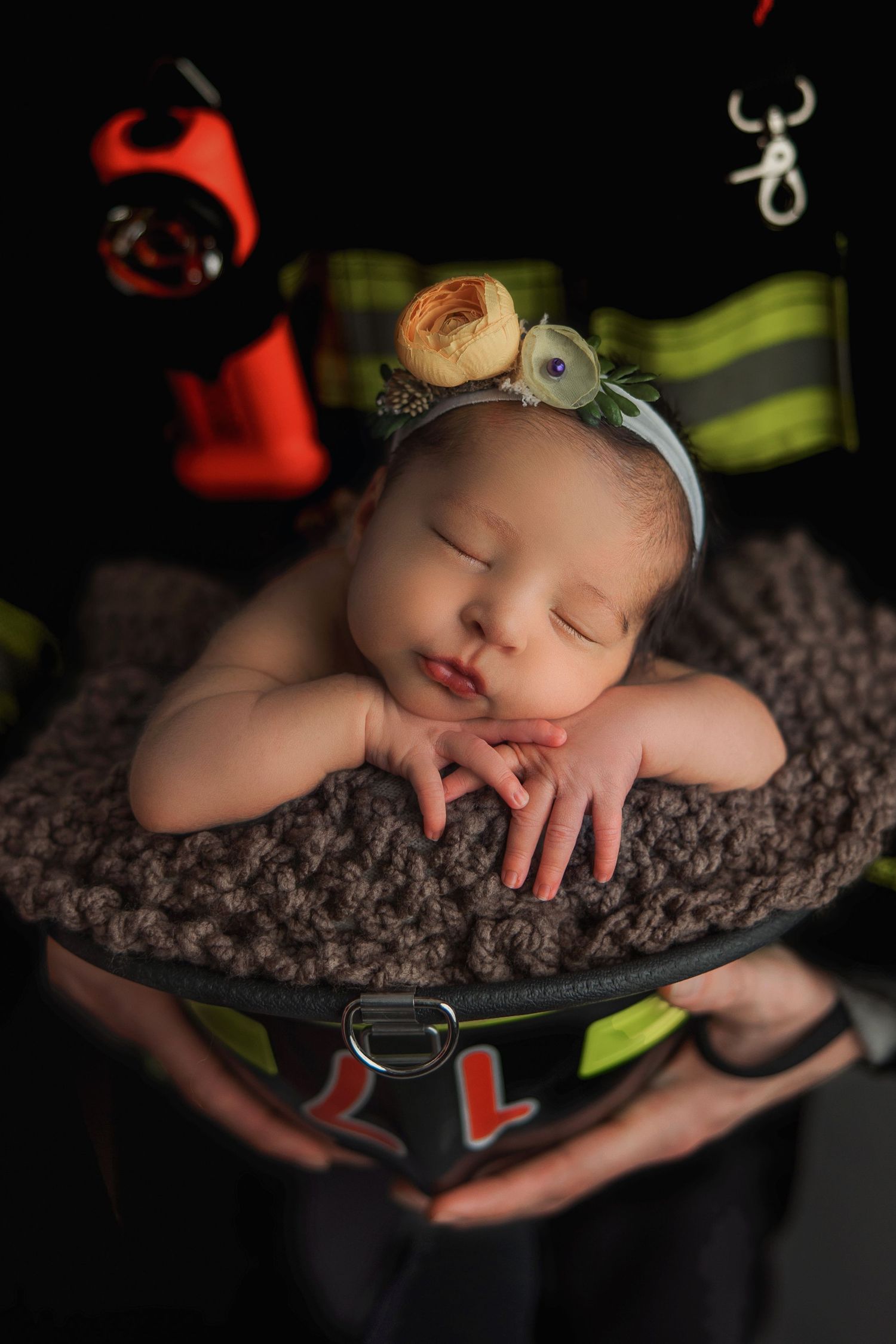 Sleeping baby dressed in firefighter gear rests peacefully on a textured brown blanket in a creative newborn photo session.