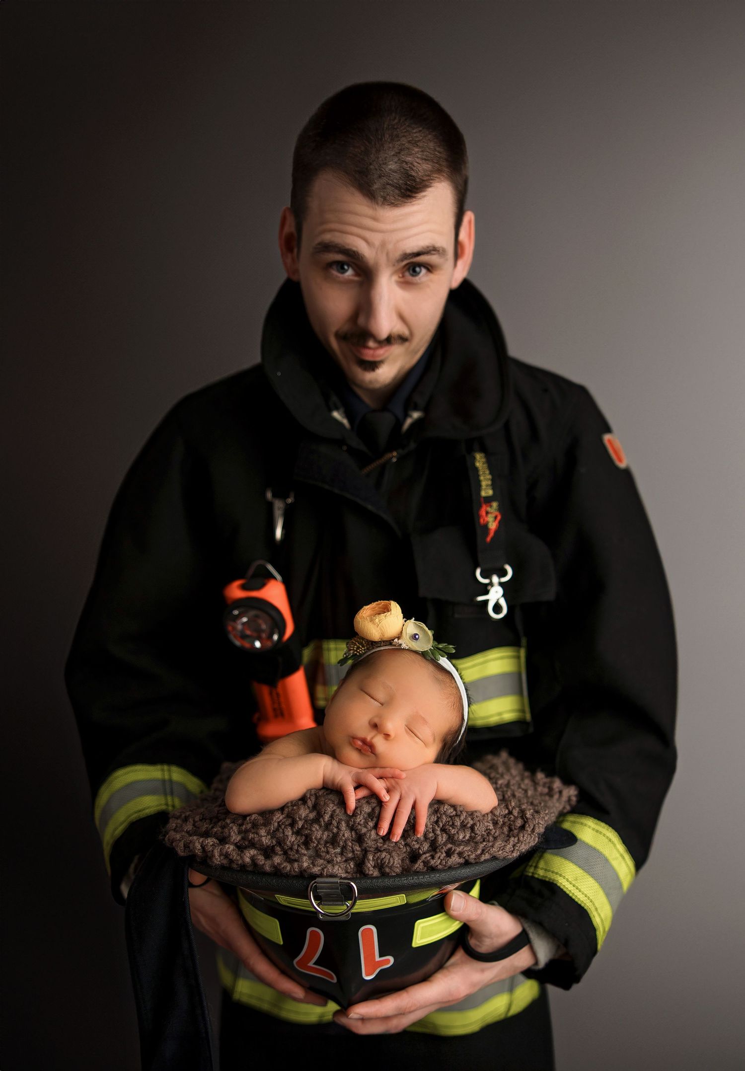 A sleeping newborn baby nestled in a firefighter's protective helmet while wearing reflective gear and uniform.