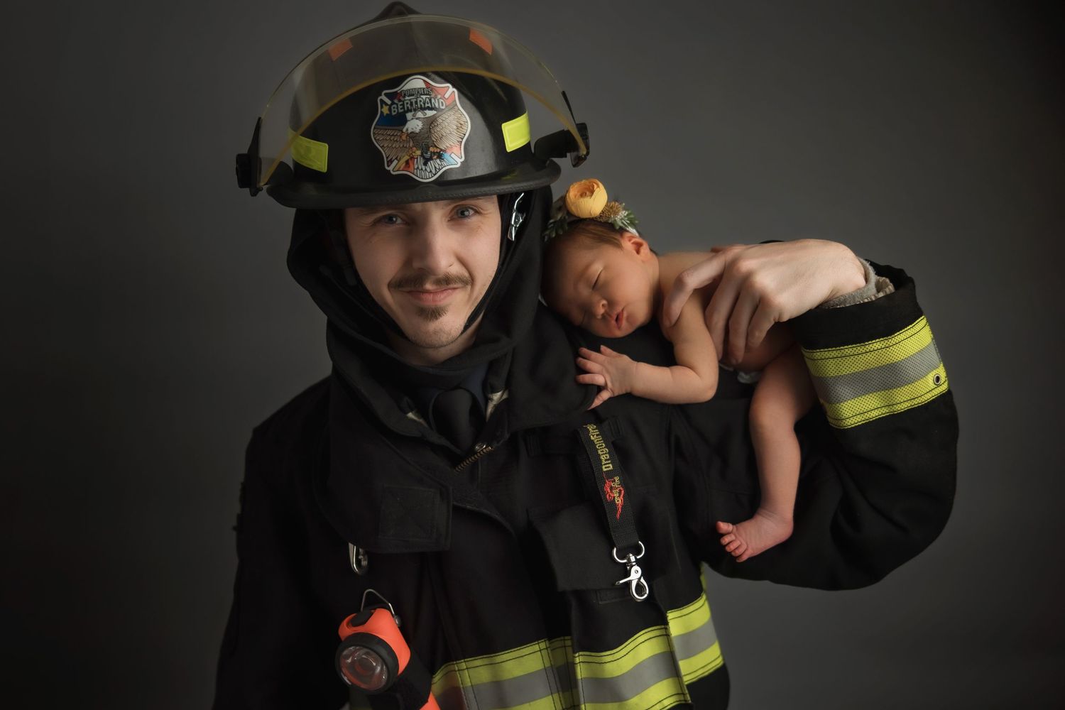A firefighter in protective gear and helmet poses against a dark background with dramatic lighting.
