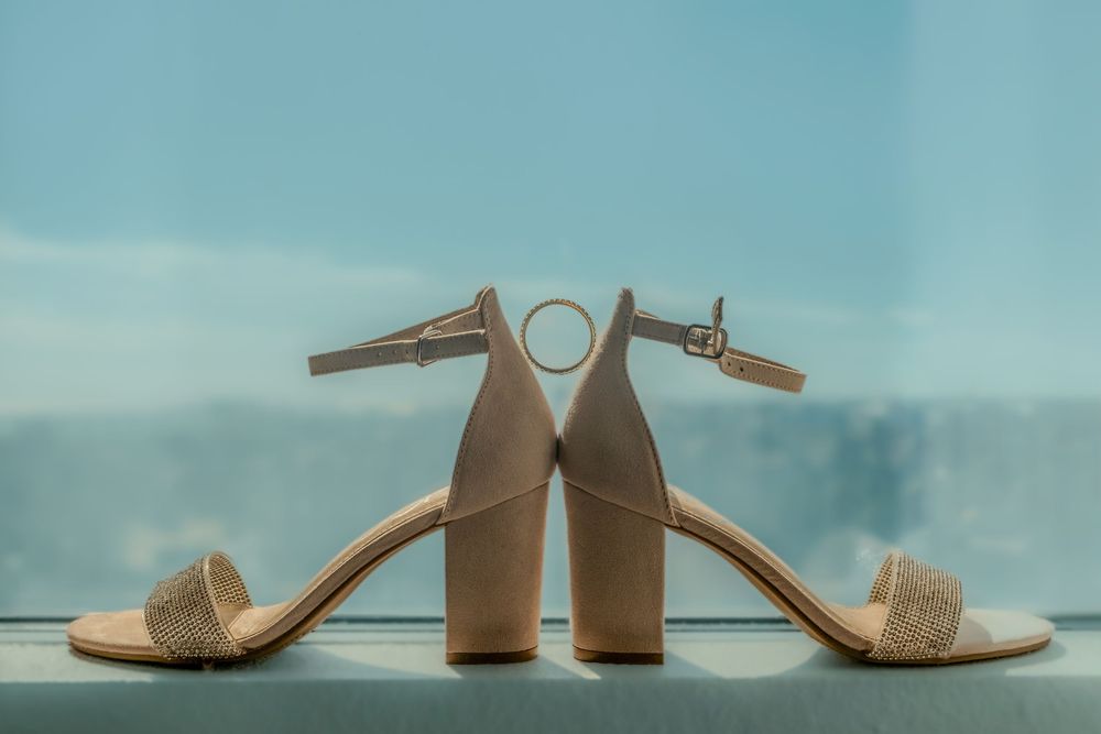 Beige suede block heel sandals with ankle straps displayed against a soft turquoise background.