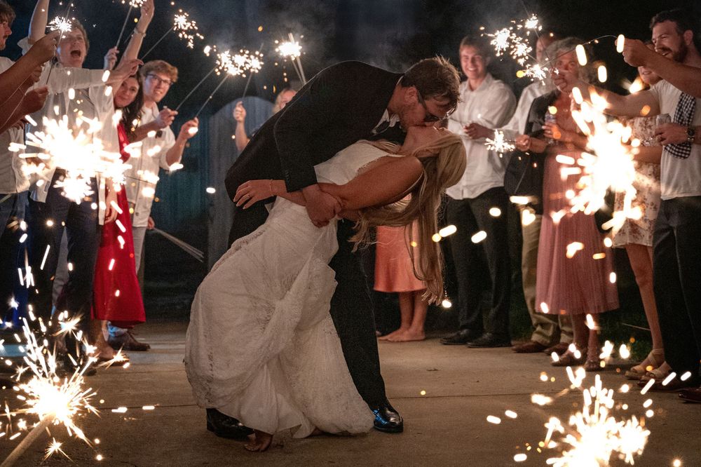 A couple shares a romantic dip during their sparkler-lit wedding sendoff surrounded by guests holding bright sparklers.