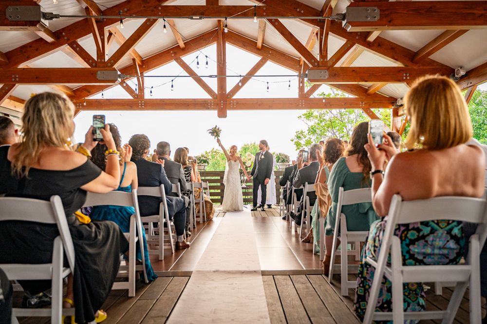 Wedding ceremony venue with exposed wooden beams and rows of white chairs filled with guests.
