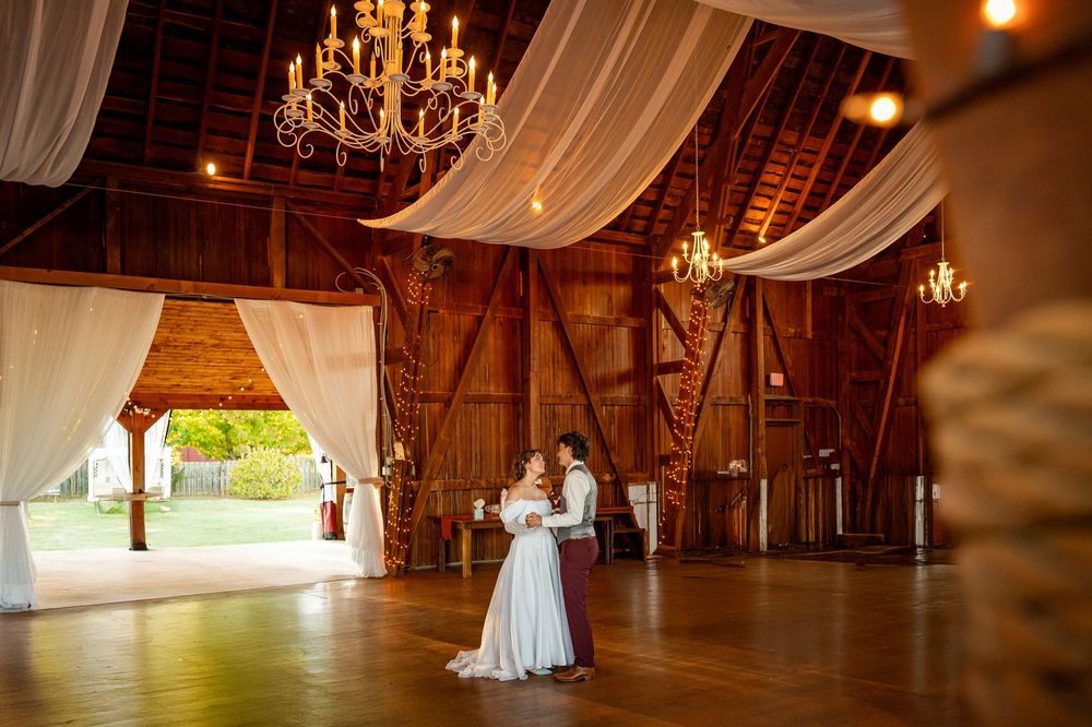 A rustic barn wedding venue with elegant chandeliers, white drapes, and warm lighting creates a romantic atmosphere.