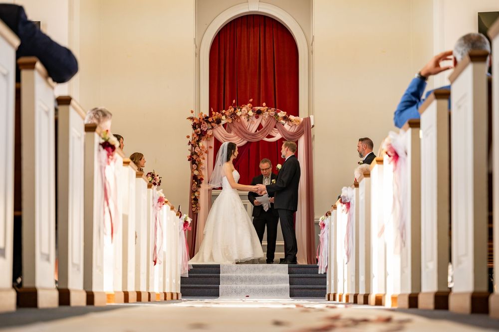 A series of arched white columns in a hallway with a red carpet runner and people walking through.
