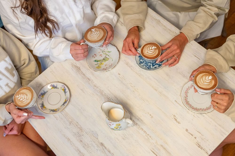 A sequence of hands creating latte art designs in coffee cups on a white surface.
